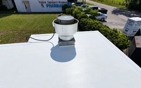 White TPO membrane on a low-slope commercial roof with a round vent, parking and a street behind