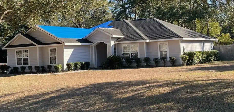 House with a blue emergency tarp covering part of its shingle roof after a storm